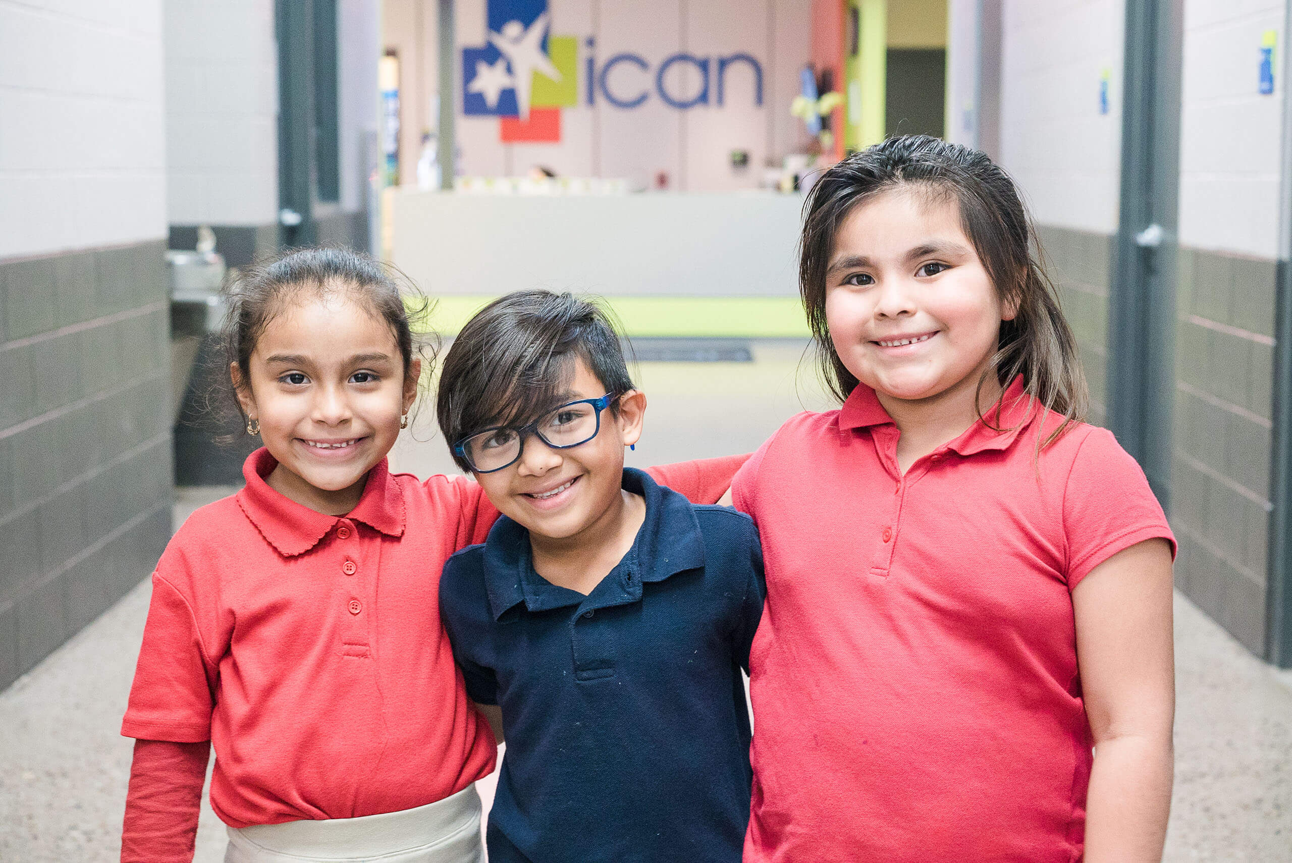 Three young kids standing smiling in the ICAN building